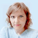 Bust portrait of Lily Edwards with short blonde hair, blue eyes, blue shirt on a sky blue background