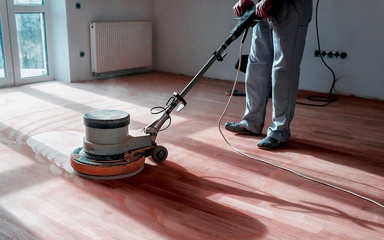 A professional worker sanding a wooden floor with a drum sanding machine